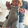 baby, child, person, adult, hat, bucket_hat, overalls, green_overalls, indoor, furniture, lamp, smiling, holding_hands, standing, learning_to_walk, home, casual_clothing, beard, man, happy