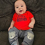 Roman is registered to the contest to win money with this photo: baby, child, smiling, red_shirt, little_brother_text, striped_pants, bear_patch, cushion, gray_background, sitting, drool, cute, indoor, comfortable, portrait, happy, infant, clothing, cozy, person