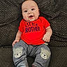 baby, child, smiling, red_shirt, little_brother_text, striped_pants, bear_patch, cushion, gray_background, sitting, drool, cute, indoor, comfortable, portrait, happy, infant, clothing, cozy, person