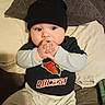 Roman is registered to the contest to win money with this photo: baby, child, infant, beanie, black_hat, clothing, bed, pillow, blanket, hands, face, cute, indoor, sitting, expression, looking_away, casual, comfort, young, portrait