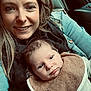 woman, baby, smile, face, person, infant, clothing, bib, denim_jacket, scarf, car_interior, window, hair, skin, eyes, nose_piercing, sitting, portrait, closeup, warmth