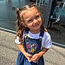 child, girl, smile, outdoor, pigtails, denim_dress, white_shirt, curly_hair, sunlight, glass_window, reflection, concrete, casual_clothing, happy, portrait, young_child, fashion, daylight, cute, standing