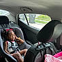 Chanel is registered to the contest to win money with this photo: black_hair, car_interior, car_seat, child, clothing, curly_hair, gift_bag, outdoor_view, person, pink_bag, portrait, red_bow, relaxed, roadside, safety, seat, seatbelt, side_view, toddler, window
