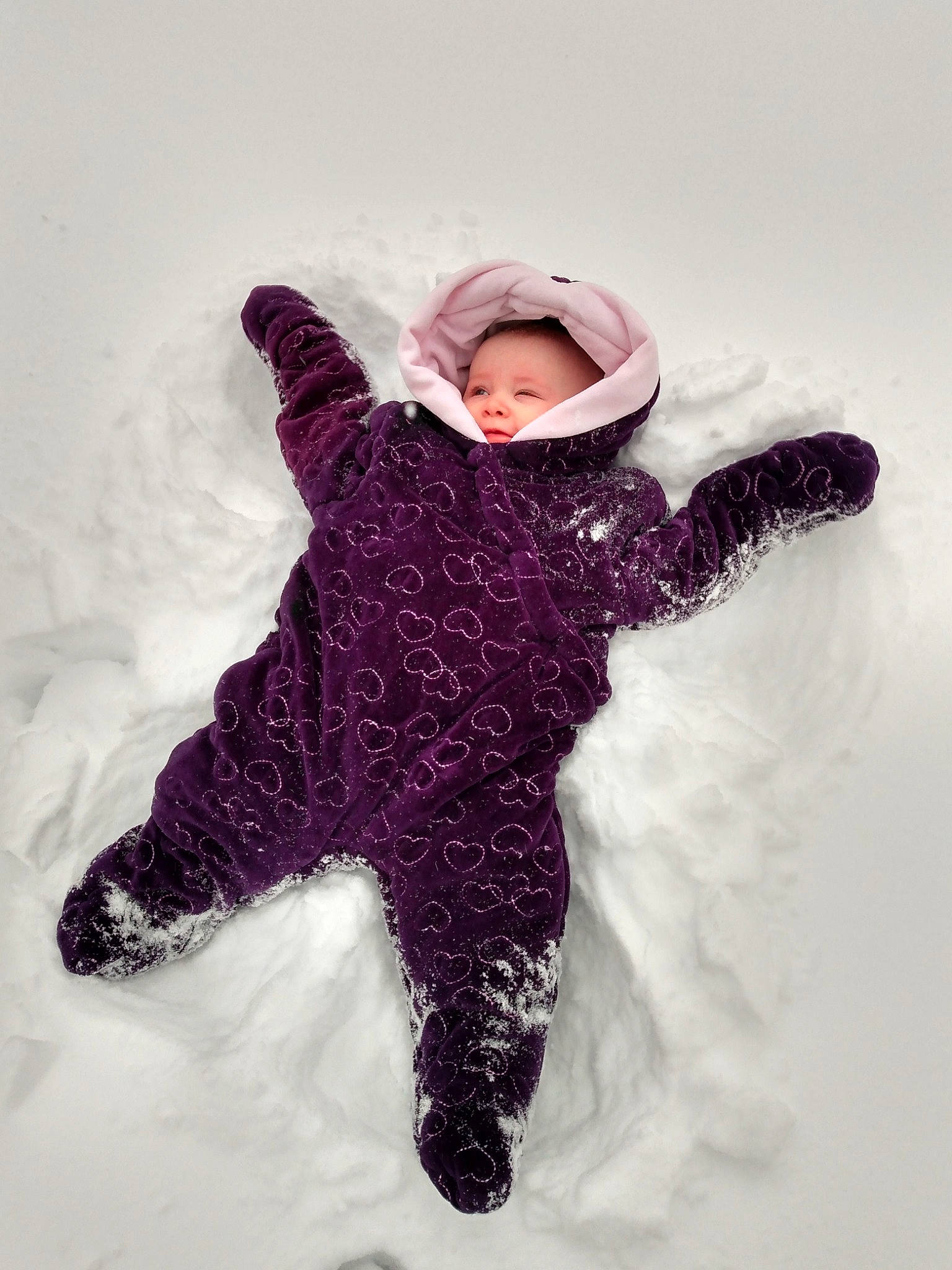 Arrow is registered to the contest to win money with this photo: baby_toddler_clothing, child, face, freezing, fur, gesture, glove, happy, hood, human_body, jacket, magenta, pattern, person, personal_protective_equipment, playing_in_the_snow, recreation, sleeve, snow, toddler