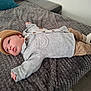 baby, infant, lying_down, knit_hat, beanie, gray_sweater, tan_pants, white_socks, blanket, bed, indoor, cute, child, soft_texture, pom_pom, portrait, resting, cozy, warm_clothing, curious