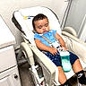 baby, infant, child, sleeping, sitting, high_chair, bottle, feeding, blue_shirt, shorts, socks, nike_socks, harness, indoor, kitchen, furniture, wall, cabinet, portrait, relaxed