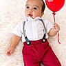 baby, child, infant, portrait, smiling, balloon, red_balloon, suspenders, white_shirt, red_pants, fashion, lying_down, fluffy_rug, indoor, studio, bright_lighting, blue_eyes, looking_away, playful, celebration