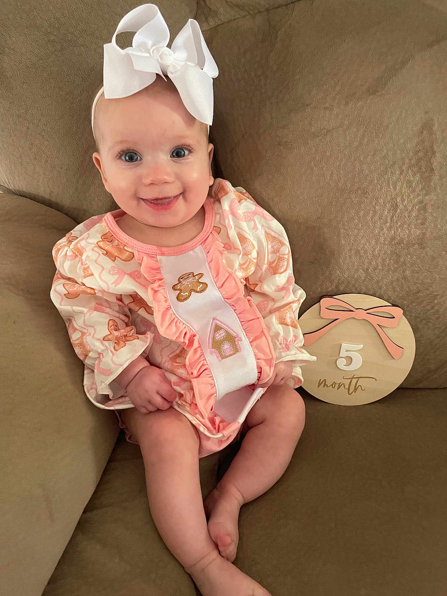 Alexandra is registered to the contest to win money with this photo: baby, infant, smile, girl, headband, bow, pink_clothing, gingerbread, couch, wooden_sign, 5_month, sitting, cute, happy, indoors, child, person, portrait, baby_girl, soft_fabric