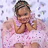 child, birthday, headband, braids, beads, pink_dress, tutu, confetti, hearts, smile, pose, celebration, cute, portrait, happy, sitting, young_girl, festive, colorful, party