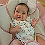 baby, smiling, infant, onesie, floral_pattern, baby_seat, cushion, pink, cream, happy, child, cute, indoors, person, portrait, skin, hand, face, head, wood_floor