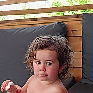 Lola participe au concours pour gagner de l'argent avec cette photo : child, toddler, curly_hair, face, outdoor, bench, cushion, wood, food, snack, expression, person, seat, relaxing, summer, natural_light, casual, young_child, portrait, bare_chest