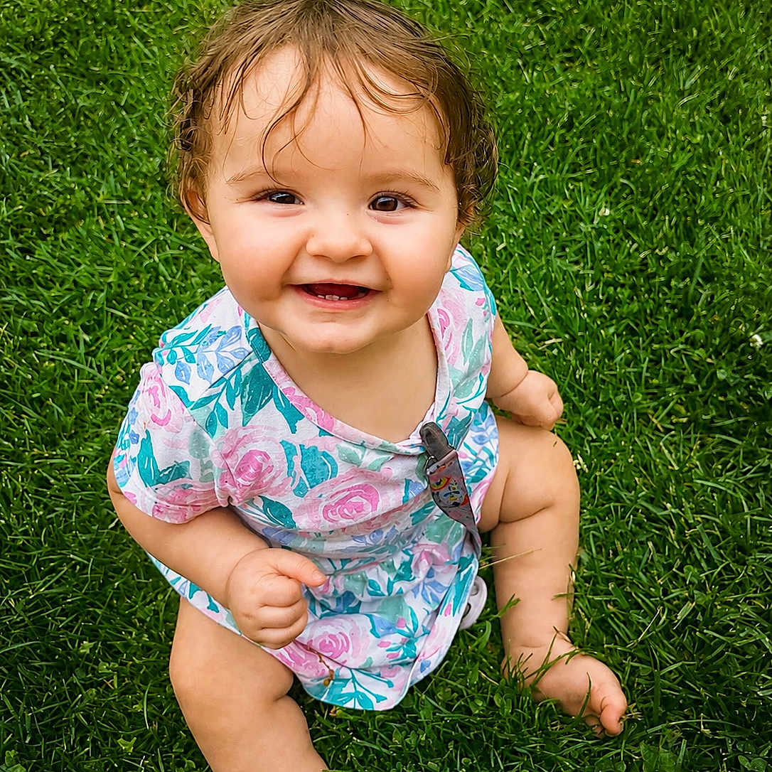 Jayliana joined the competition — help win amazing prizes! baby, child, grass, smile, happy, sitting, outdoor, floral_dress, curly_hair, cute, young_child, nature, barefoot, greenery, portrait, face, skin, summer, playful, innocent