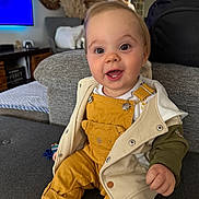 Camille participe au concours pour gagner de l'argent avec cette photo : baby, child, smiling, overalls, jacket, couch, indoor, living_room, happy, person, face, clothing, sitting, cute, infant, casual, home, portrait, young_child, cozy