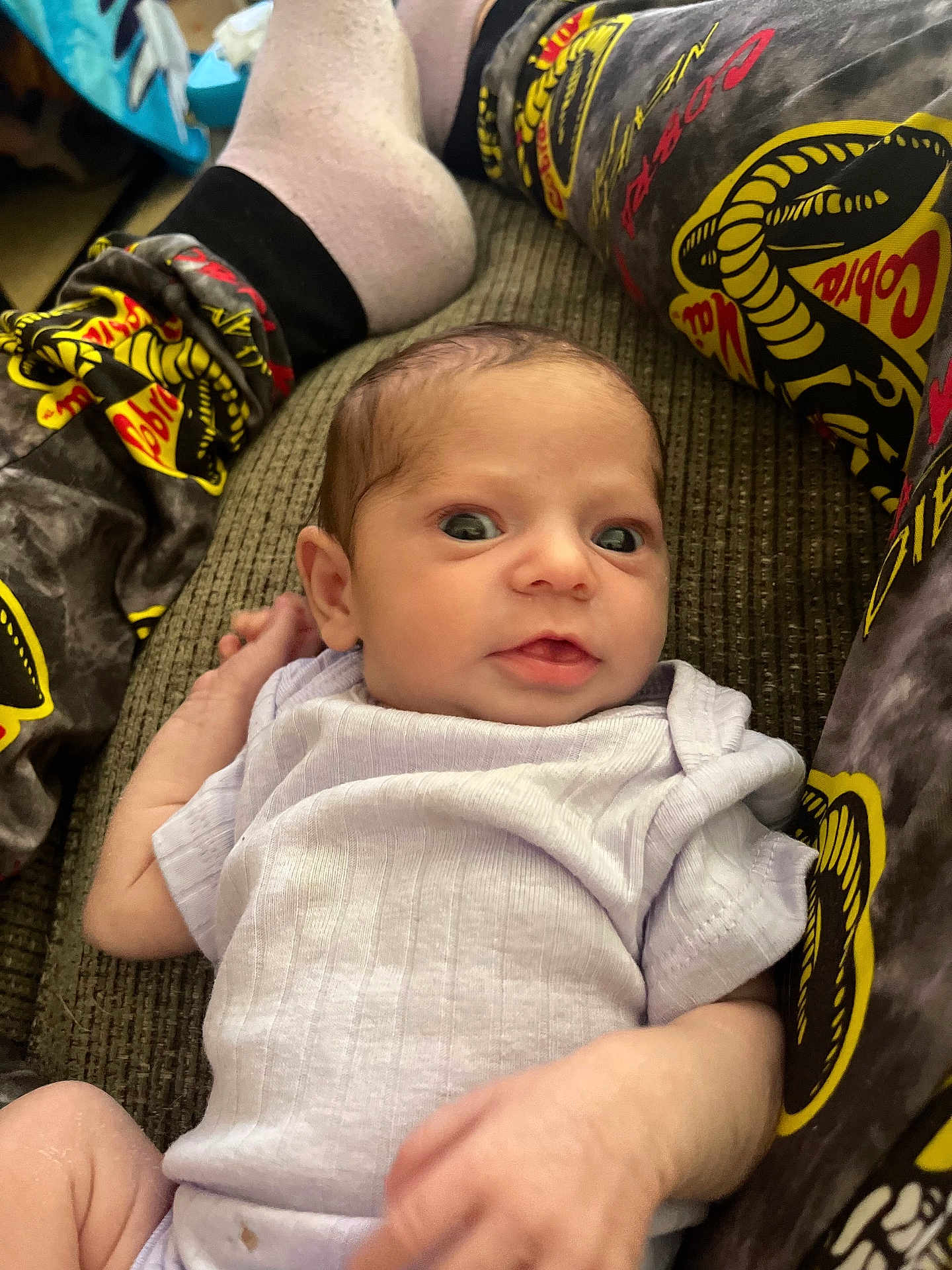 Grace is registered to the contest to win money with this photo: baby, infant, couch, clothing, onesie, person, legs, socks, patterned_pants, snake_pattern, texture, indoor, portrait, young_child, cute, wide_eyes, resting, hand, fabric, casual