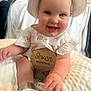 Iris is registered to the contest to win money with this photo: baby, infant, child, smiling, hat, floral_clothing, wooden_sign, seven_months, sitting, blanket, shoes, cute, indoors, happy, portrait, person, small_hands, closeup, soft_lighting, headwear