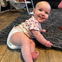 Iris joined the competition — help win amazing prizes! baby, child, diaper, smiling, sitting, floor, rug, wooden_floor, living_room, baby_swing, couch, toy, happy, cute, infant, playful, casual_clothing, indoor, person, portrait