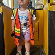 Ophelía joined the competition — help win amazing prizes! toddler, child, safety_vest, birthday_shirt, shorts, shoes, socks, indoor, yellow, industrial, play_area, curious, standing, person, window, floor, pipe, expression, clothing, lighting