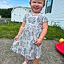 cartoon_pattern, casual_clothing, child, concrete, cute, daylight, dress, footwear, grass, happy, mobile_home, outdoor, person, pink_shoes, playground, portrait, shed, smiling, toddler, young_child