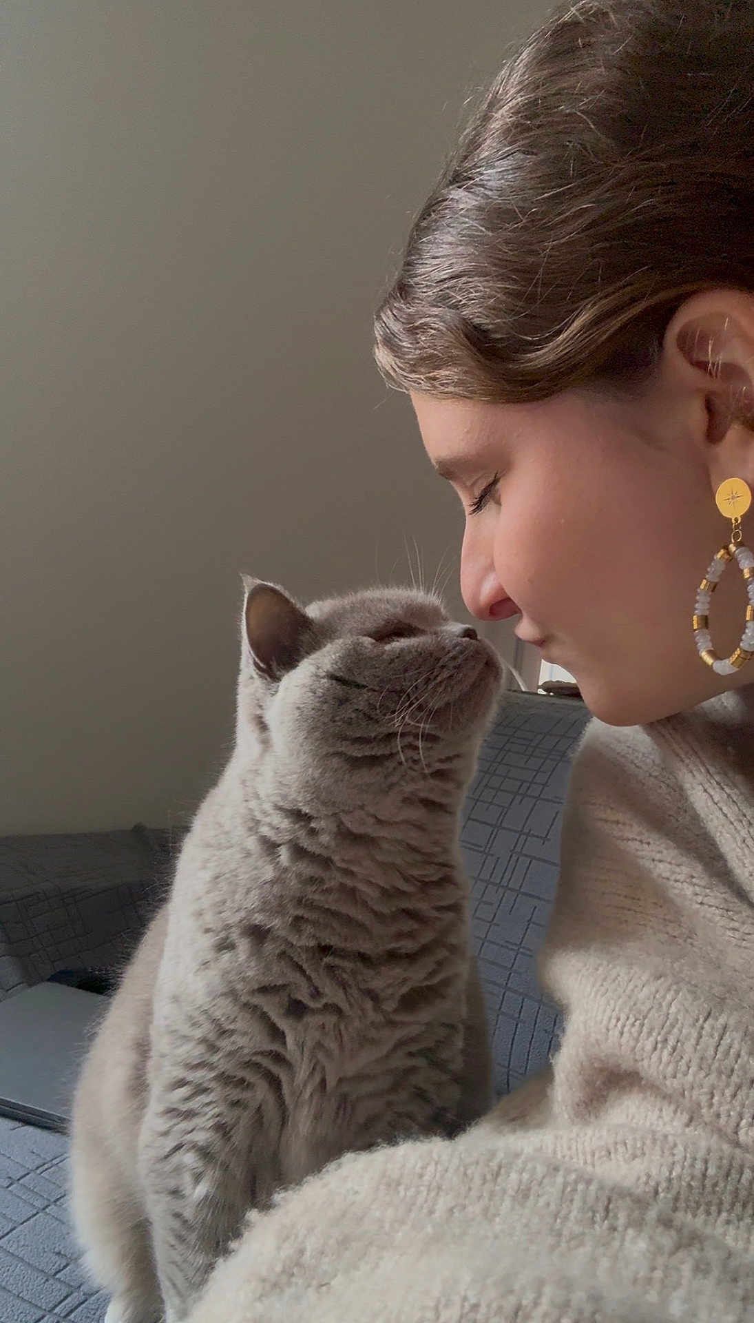 Oïana participe au concours pour gagner de l'argent avec cette photo : cat, person, face, nose_to_nose, gray_cat, indoor, couch, earring, sweater, closeup, pet, affection, feline, human, whiskers, fur, cozy, intimate, soft_light, portrait