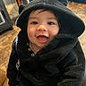 baby, child, hoodie, black_clothing, smiling, happy, indoor, cute, face, eyes, button, furniture, floor, person, portrait, warm_lighting, cozy, infant, young_child, clothing