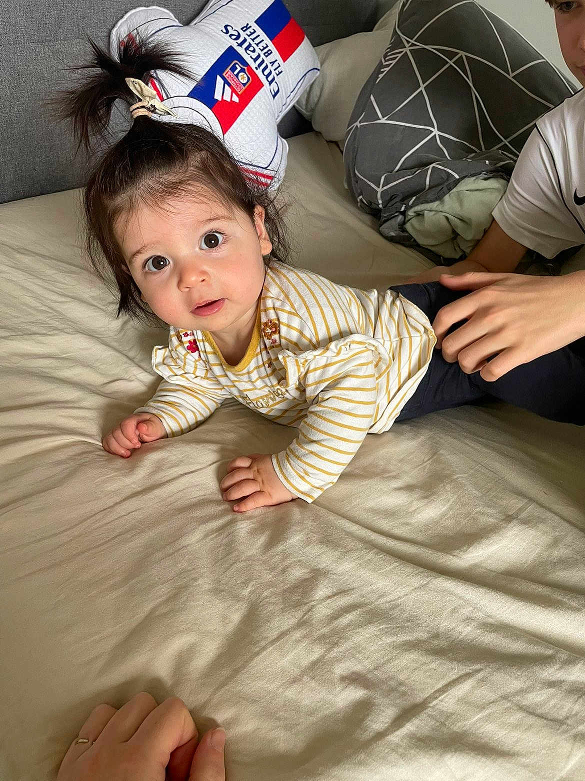Giulia participe au concours pour gagner de l'argent avec cette photo : child, baby, bed, pillow, bedding, striped_shirt, big_eyes, hair_tie, smile, hands, person, portrait, indoor, playful, sibling, blanket, couch, casual_clothing, curious, soft_light