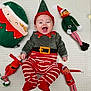 baby, smiling, elf_costume, red_and_white_stripes, green_clothing, holiday, christmas, plush_toys, elf_dolls, pillow, happy, infant, lying_down, cute, festive, indoor, child, toy, face, red_hat