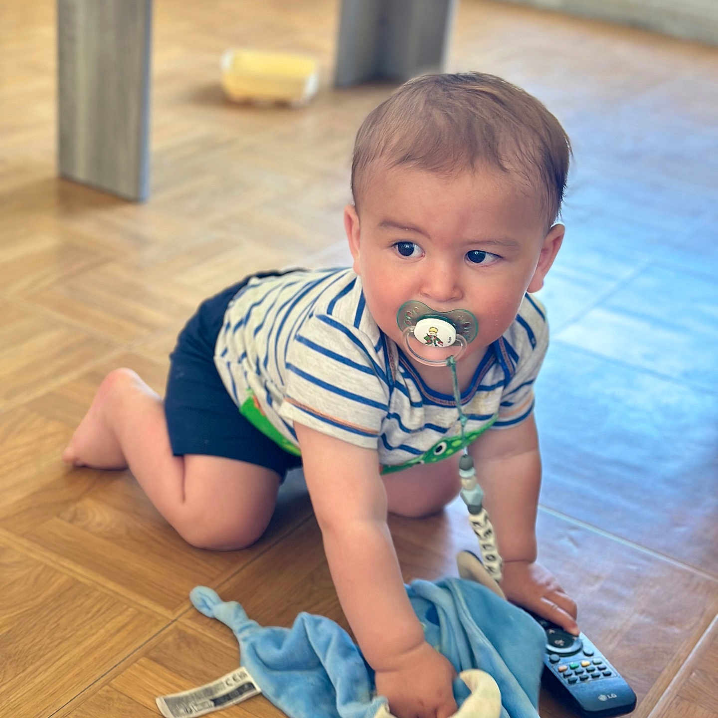 Kelohann a rejoint le concours — aidez-le/la à gagner de superbes lots ! baby, blue_blanket, child, clothing, crawling, curious, cute, flooring, home, indoors, infant, pacifier, person, playful, remote_control, striped_shirt, toddler, toy, wooden_floor, young_child