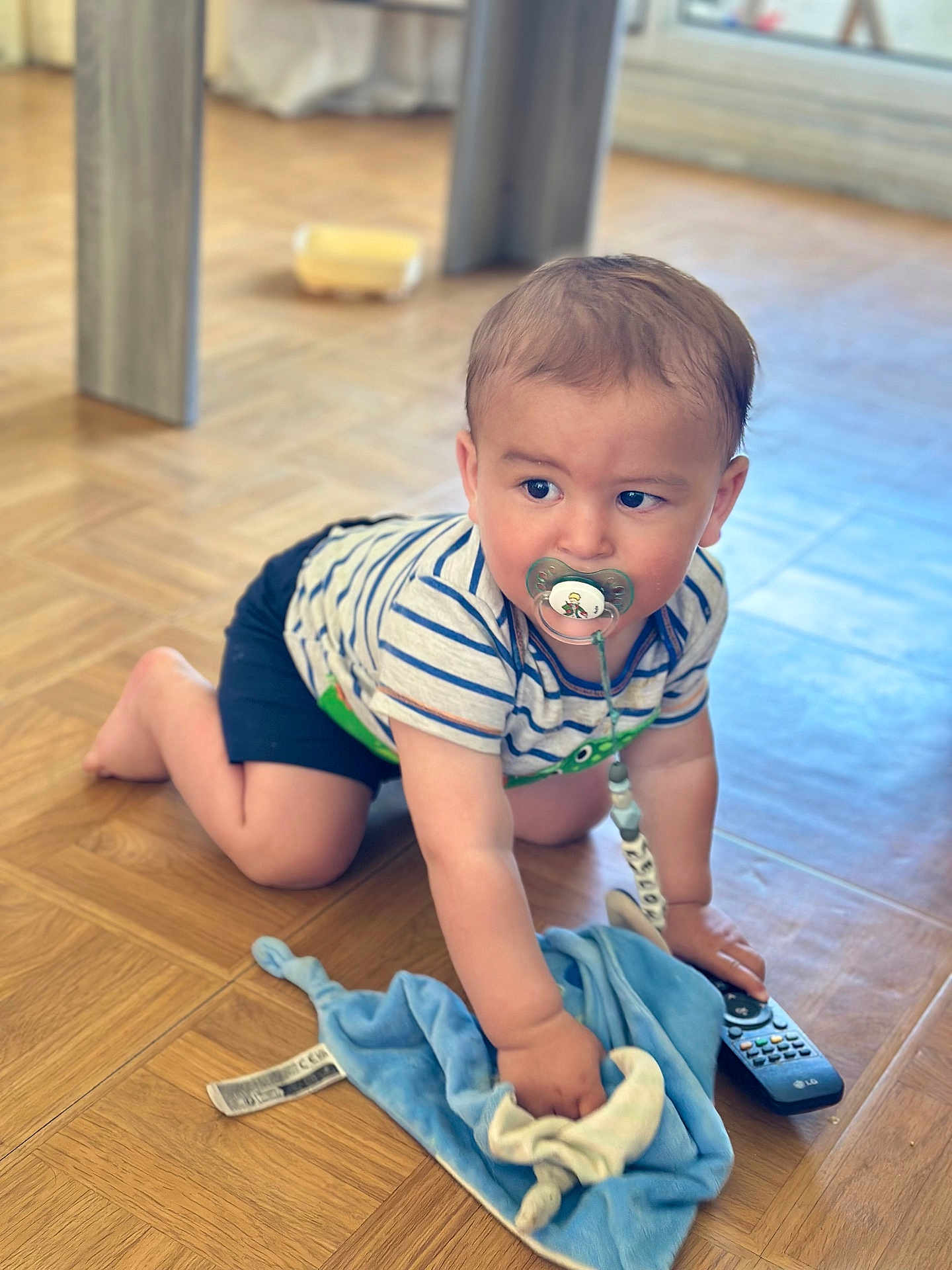 Kelohann a rejoint le concours — aidez-le/la à gagner de superbes lots ! baby, crawling, pacifier, striped_shirt, blue_blanket, remote_control, wooden_floor, indoors, child, cute, toddler, toy, flooring, clothing, person, young_child, home, curious, infant, playful