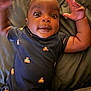 Khalid is registered to the contest to win money with this photo: baby, child, infant, onesie, teddy_bear_pattern, cushion, couch, smiling, face, arms_up, wide_eyes, indoor, cute, person, portrait, happy, skin, curly_hair, lying_down, closeup
