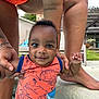 Khalid is registered to the contest to win money with this photo: baby, child, person, orange_clothing, swimsuit, holding_hands, outdoor, poolside, smile, face, tattoo, barefoot, summer, cute, infant, playful, sunny, background, expression, supporting_hands