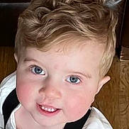 Lorenzo is registered to the contest to win money with this photo: child, boy, curly_hair, blonde_hair, blue_eyes, smiling, white_shirt, suspenders, indoor, wooden_floor, leather_couch, face, portrait, cute, happy, looking_up, young, person, closeup, childhood