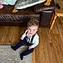 Lorenzo is registered to the contest to win money with this photo: child, toddler, smiling, indoor, wooden_floor, couch, cushion, pillow, clothing, suspenders, face, person, home, carpet, remote_control, furniture, happy, curly_hair, sitting, floor