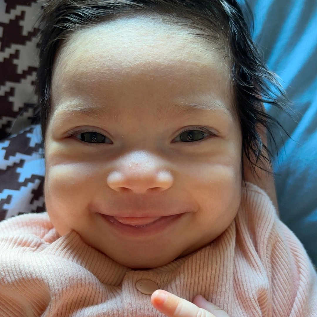 Khalyssa a rejoint le concours — aidez-le/la à gagner de superbes lots ! baby, blanket, child, closeup, cute, dark_hair, face, hands, happy, indoors, infant, lying_down, patterned_blanket, person, pink_clothing, portrait, ribbed_fabric, skin, smiling, soft_light