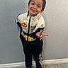 child, boy, smiling, portrait, standing, peace_sign, racing_suit, jumpsuit, sportswear, sneakers, indoor, wall, floor, fashion, happy, pose, short_hair, full_body, casual, photography