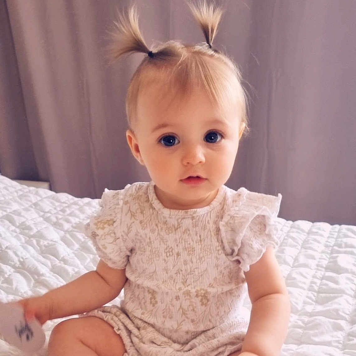 Milyana a rejoint le concours — aidez-le/la à gagner de superbes lots ! baby, bed, blonde_hair, blue_eyes, child, clothing, curious, cute, cute_outfit, expression, hands, indoor, infant, person, pigtails, portrait, quilt, sitting, soft_lighting, young_child