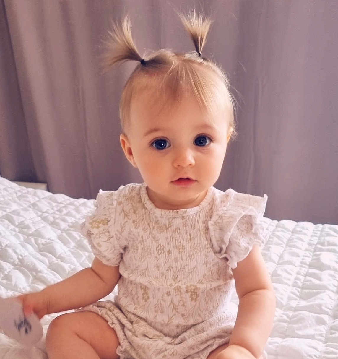 Milyana a rejoint le concours — aidez-le/la à gagner de superbes lots ! baby, child, infant, portrait, cute, pigtails, blonde_hair, blue_eyes, sitting, bed, quilt, clothing, indoor, soft_lighting, curious, young_child, person, cute_outfit, expression, hands