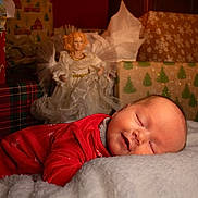 Blair is registered to the contest to win money with this photo: baby, sleeping, red_clothing, blanket, christmas, presents, angel_figurine, holiday, festive, cozy, infant, portrait, indoors, decor, cute, peaceful, soft, warm, smiling, relaxing