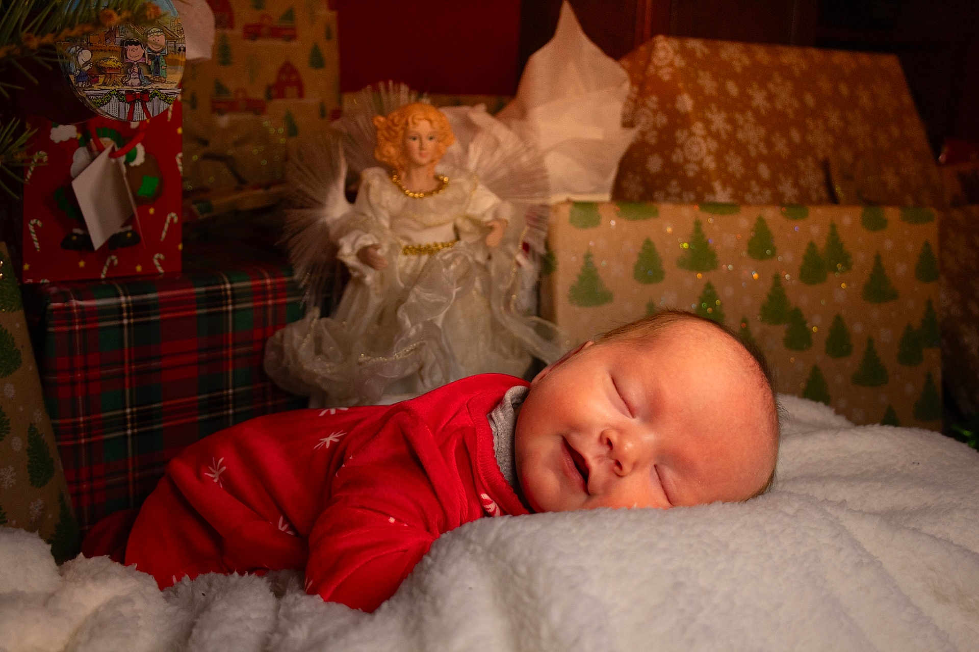 Blair is registered to the contest to win money with this photo: baby, sleeping, red_clothing, blanket, christmas, presents, angel_figurine, holiday, festive, cozy, infant, portrait, indoors, decor, cute, peaceful, soft, warm, smiling, relaxing
