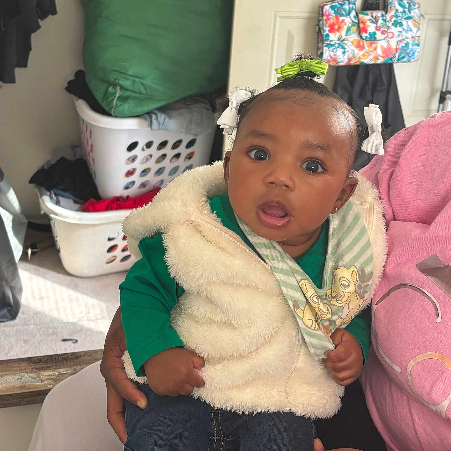 Janiyah is registered to the contest to win money with this photo: baby, bag, casual, child, clothing, curious, cute, expression, green_shirt, hair_bow, hand, holding, indoor, jeans, laundry_basket, person, portrait, seated, vest, young