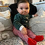baby, infant, child, couch, pillow, cushion, blanket, striped_leggings, red_booties, green_top, buttons, sitting, cute, chubby_cheeks, big_eyes, living_room, fuzzy_throw, wall_decor, hand, portrait