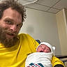 Christopher joined the competition — help win amazing prizes! man, newborn, baby, hospital, blanket, yellow_shirt, person, indoor, smile, beard, hat, swaddle, happy, portrait, family, child, care, love, parent, rest