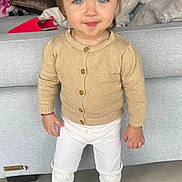 Alba a rejoint le concours — aidez-le/la à gagner de superbes lots ! blue_eyes, cardigan, child, couch, cozy, cute, fashion, floor_tiles, home, indoor, living_room, person, pony_tail, portrait, smiling, socks, standing, toddler, white_pants, young_child