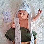 Ediz a rejoint le concours — aidez-le/la à gagner de superbes lots ! baby, infant, hat, knitted, blanket, milestone_card, one_month, lying_down, cute, serious_face, child, soft_texture, green_cloth, woven_basket, newborn, portrait, indoor, skin, hand, expression