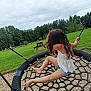child, swing, park, grass, trees, rope_swing, barefoot, curly_hair, summer_clothing, shorts, tank_top, playground, outdoor, nature, greenery, picnic_table, cloudy_sky, recreation, fun, leisure