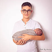 Henzo participe au concours pour gagner de l'argent avec cette photo : boy, baby, child, newborn, glasses, white_shirt, swaddled, holding, portrait, studio, smile, person, hands, infant, family, sibling, cute, young, indoor, soft_lighting