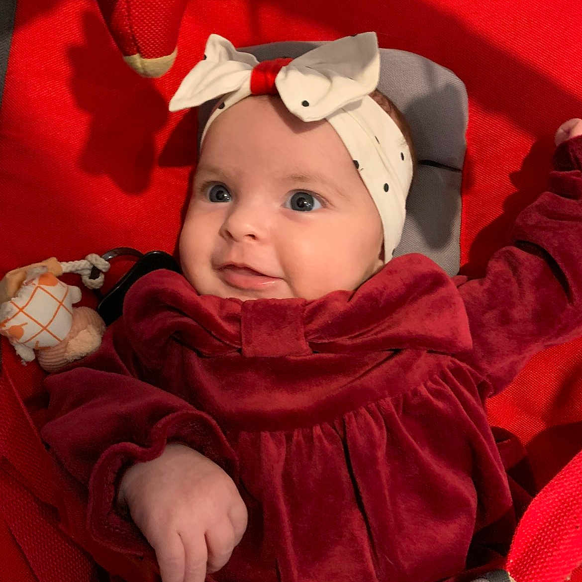 Violette participe au concours pour gagner de l'argent avec cette photo : baby, blue_eyes, bow, child, cozy, cushion, cute, hand, happy, headband, indoor, infant, person, portrait, red_clothing, seat, smile, soft_toy, toy, velvet