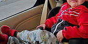 Romeo is registered to the contest to win money with this photo: child, car_seat, red_jacket, pants, airplane_print, sneakers, seatbelt, car_interior, window, rain_drops, face, expression, funny_face, sitting, casual, indoor, person, clothing, transportation, daylight