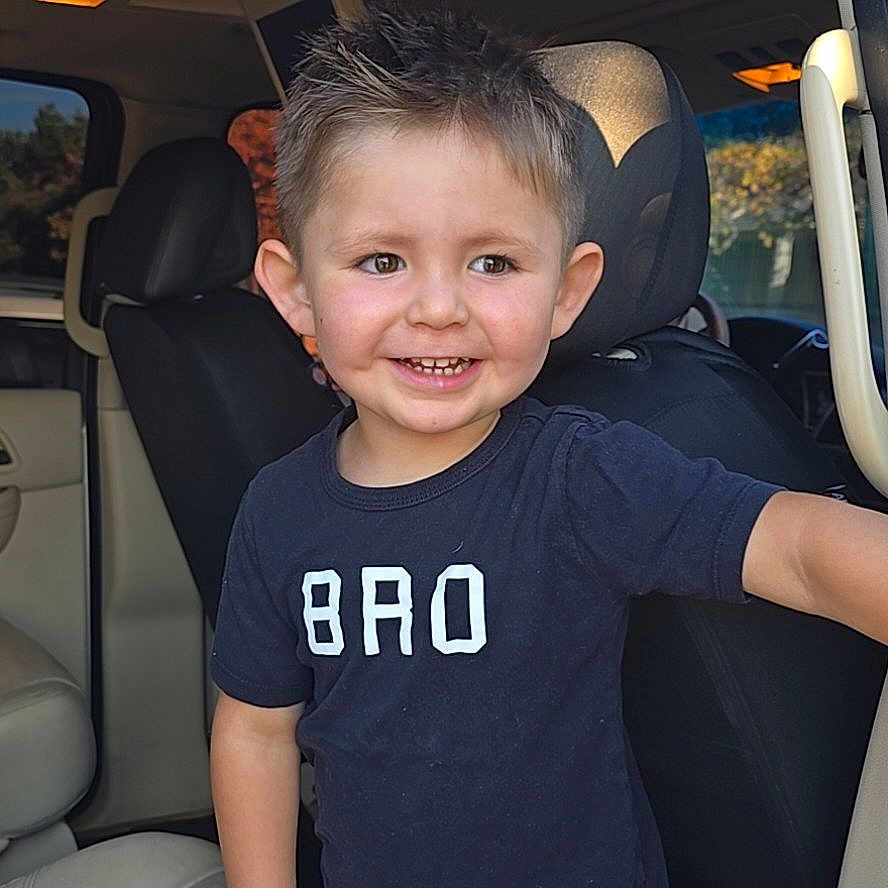 Romeo is registered to the contest to win money with this photo: automobile, boy, bro, car_interior, casual_clothing, child, cute, daylight, door, happy, indoors, person, portrait, seat, seatbelt, short_hair, smile, tshirt, window, young