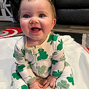 Chloe joined the competition — help win amazing prizes! baby, infant, smiling, clothing, onesie, pattern, clover, milestone, wooden_marker, blanket, sitting, happy, indoor, floor, couch, furniture, child, cute, portrait, person