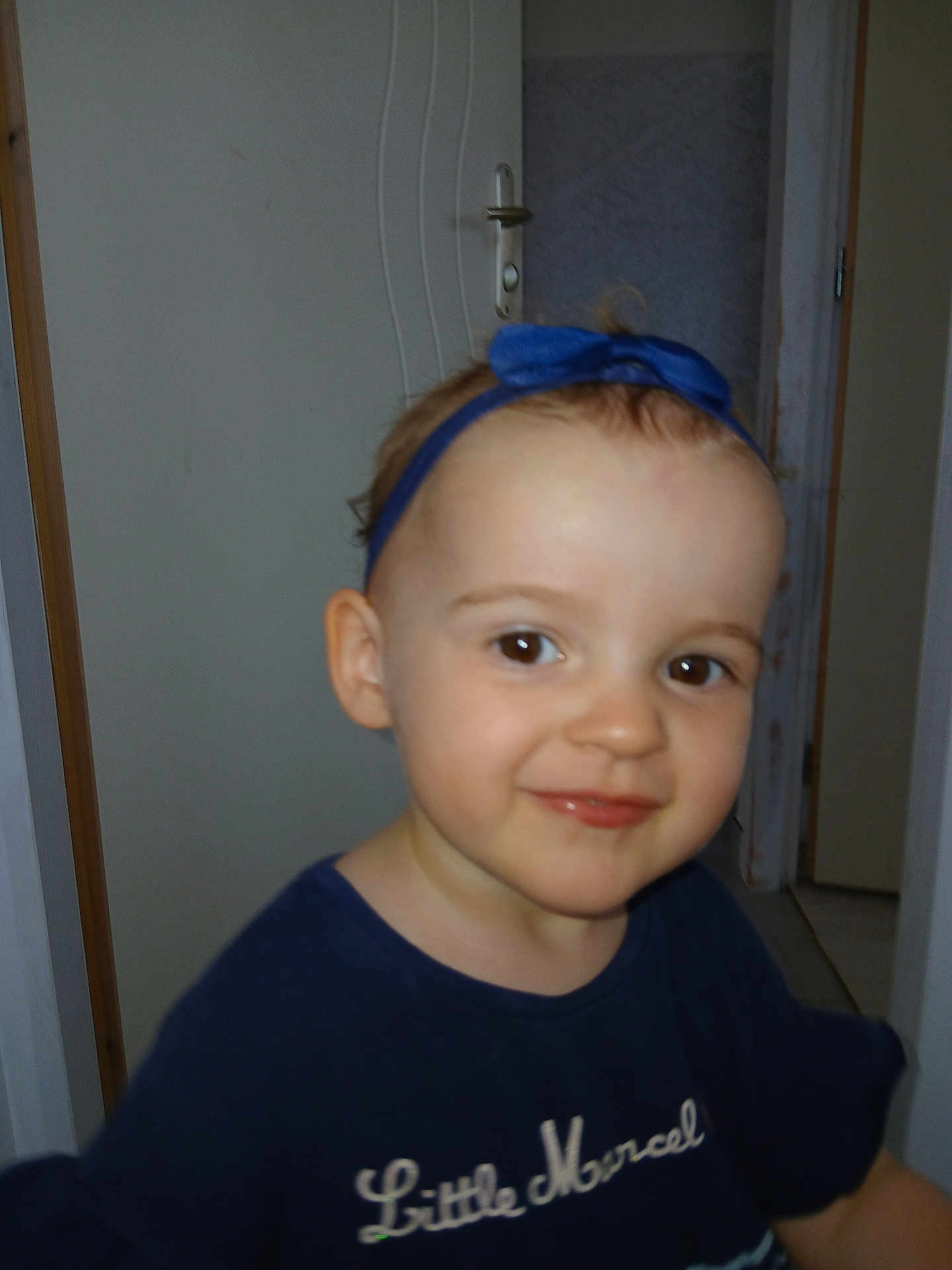 Cyndel participe au concours pour gagner de l'argent avec cette photo : toddler, child, blue_headband, blue_shirt, smile, face, indoor, door, person, young_child, headband, clothing, portrait, cute, standing, expression, baby, human, skin, happy